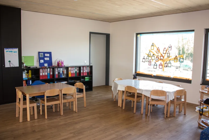 Gruppenraum mit Tischen, Regalen und einem bemalten Fenster